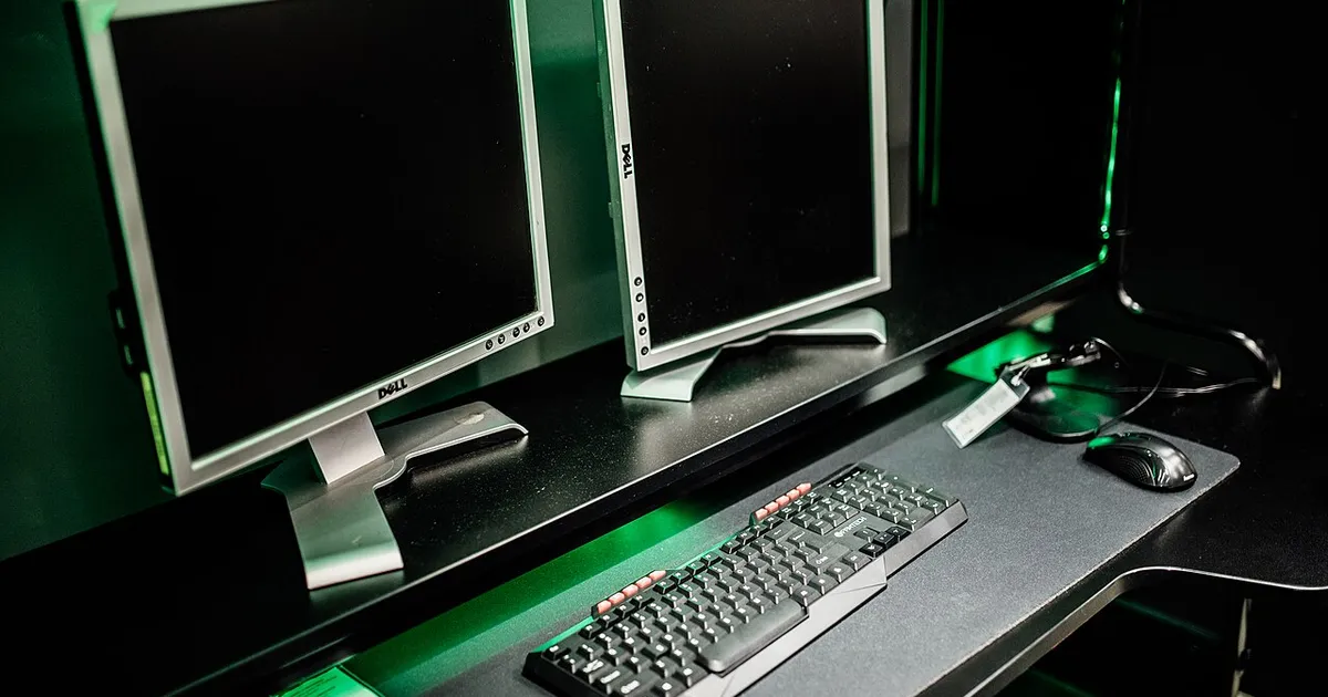 Two monitors on a gaming desk with a backlit keyboard and mouse